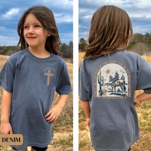 May include: A denim blue t-shirt with a brown cross and the text "Proverbs 3:5-6" on the front. The back of the shirt features a brown illustration of a cowboy riding a horse in a desert landscape with the text "Trust in the Lord with all your heart and He will direct your paths" and "Proverbs 3:5-6".