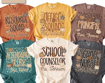 May include: Six short-sleeved t-shirts in various colors including rust, yellow, brown, teal, cream, and charcoal. Each shirt features a leopard print background with pumpkin graphics and text identifying school roles like Resource Squad and School Nurse.
