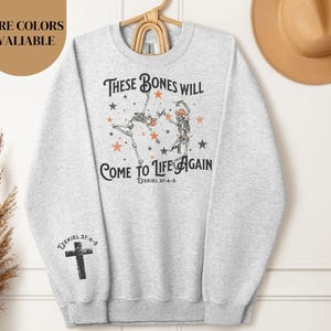 May include: Gray sweatshirt with a graphic of two skeletons dancing with the text "These bones will come to life again Ezekiel 37:4-5".