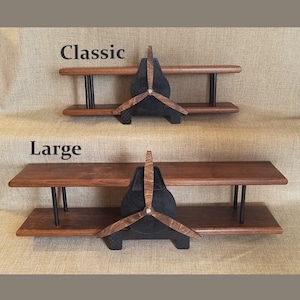 May include: Two wooden airplane-shaped shelves, one labeled "Classic" and the other "Large." Each shelf has two levels and a propeller design. The shelves are made of dark wood with black accents and are displayed against a neutral background.