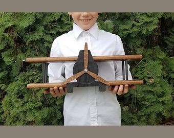 May include: A wooden airplane shelf unit with a black propeller and brown wood wings. The shelf unit is being held by a person.