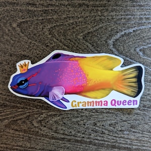 Könnte beinhalten: Ein lila und gelber Fisch mit einem rosa Streifen und einer goldenen Krone auf dem Kopf. Der Fisch schwimmt nach rechts und der Text "Gramma Queen" befindet sich darunter.