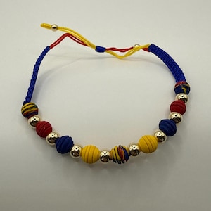 May include: A vibrant bracelet with alternating red, blue, and yellow beads, separated by silver-coloured beads. The bracelet is strung on a blue cord with yellow and red detailing, creating a striking and colourful accessory.