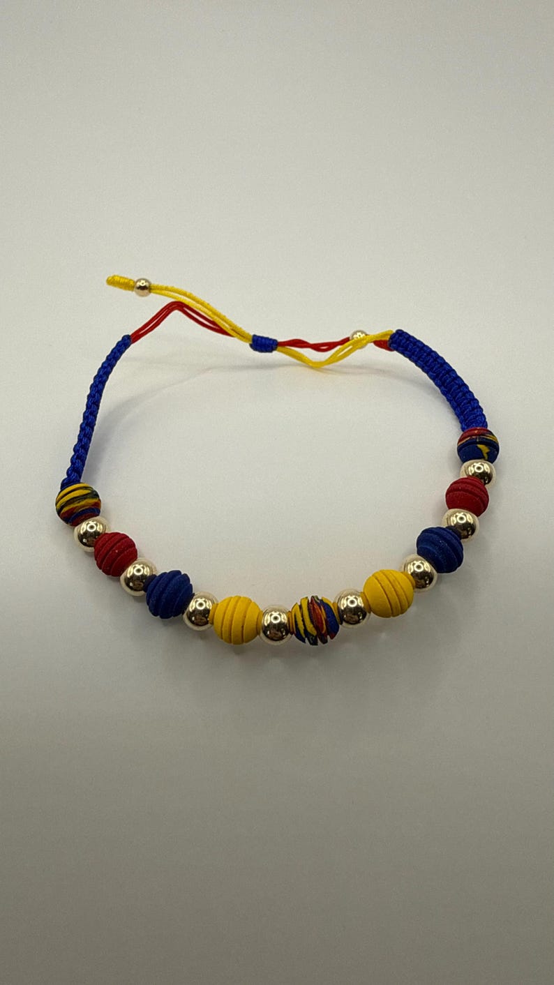 May include: A vibrant bracelet with alternating red, blue, and yellow beads, separated by silver-coloured beads. The bracelet is strung on a blue cord with yellow and red detailing, creating a striking and colourful accessory.