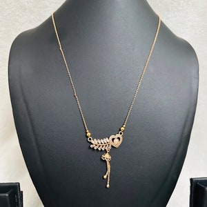 May include: A gold-tone necklace with a heart-shaped pendant adorned with clear stones. The pendant features a dangling charm with a small pearl and clear stones.