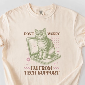 May include: A beige t-shirt with a green cat sitting on a laptop. The text on the shirt reads "Don't Worry I'm From Tech Support".
