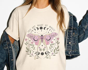 May include: A cream colored t-shirt with a pink butterfly graphic and the text "You are made of magic" in a circle around the butterfly.