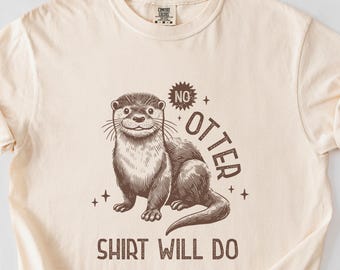 Puede incluir: Una camiseta beige con una ilustración marrón de una nutria y el texto "No otter shirt will do."