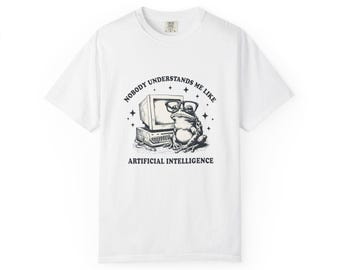 May include: White t-shirt featuring a black and white graphic of a frog wearing glasses sitting in front of a computer. The text reads "NOBODY UNDERSTANDS ME LIKE ARTIFICIAL INTELLIGENCE."