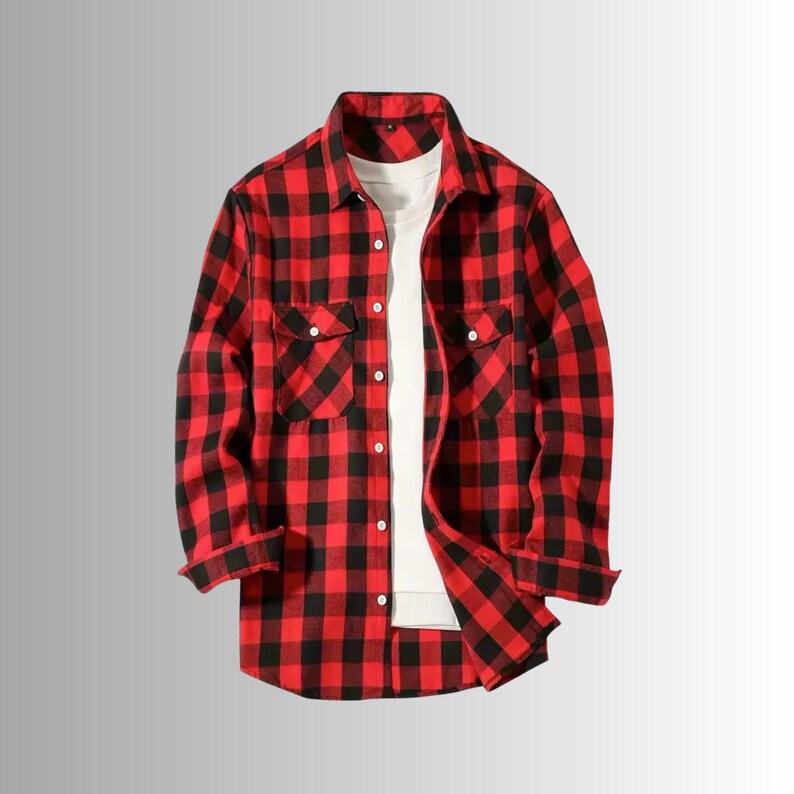 May include: A red and black plaid flannel shirt with two chest pockets and a button-down front. A white t-shirt is visible underneath. The sleeves are rolled up. The shirt is displayed on a gradient gray background.