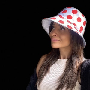 May include: A white bucket hat with red polka dots. The hat is worn by a person with long brown hair.