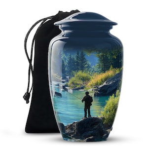 May include: A navy blue cremation urn featuring a scenic landscape of a fisherman on a river. The urn has a glossy finish and a matching lid. A black drawstring bag is next to the urn.