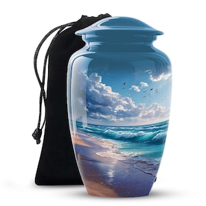May include: A blue cremation urn with a glossy finish, featuring a serene beach scene with waves, clouds, and birds. A black drawstring bag is next to the urn. The urn is designed to hold the ashes of a loved one.