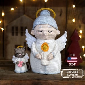 May include: Crocheted angel figurine with a halo, wings, and a candle-like design. A smaller crocheted cat figurine with wings and a heart is next to the angel. The image includes the text "EN PDF CROCHET PATTERN".