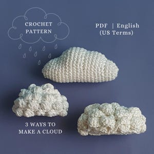 Op de afbeelding: Drie witte gehaakte wolkvormen op een blauwe achtergrond. De afbeelding bevat de tekst "CROCHET PATTERN" en "3 WAYS TO MAKE A CLOUD". De tekst "PDF | English (US Terms)" is ook zichtbaar.