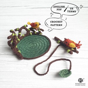 May include: A crochet pattern featuring a circular green base with brown branches and small yellow and orange birds. Text bubbles include English PDF, US Terms, and Crochet Pattern. A separate brown cord with a green leaf is attached to a bird.