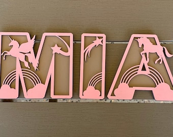 May include: Pink wooden letters spelling "MIA" with a unicorn, rainbow, and star cutouts.