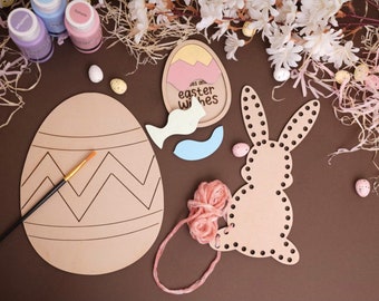 May include: A craft kit for making Easter decorations. It includes a wooden egg with a chevron pattern, a wooden bunny with holes for stringing yarn, a wooden egg with the words "Say our Easter wishes", and a small paintbrush. The kit also includes paint, yarn, and small plastic eggs.