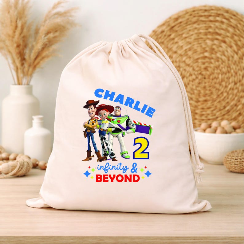 Pu&ograve; includere: Una sacca beige con coulisse con una grafica colorata di Woody, Jessie e Buzz Lightyear. La sacca ha il nome "Charlie" in blu, il numero "2" in giallo e la frase "infinity & beyond".