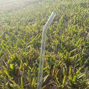 May include: A clear glass drinking straw with a slight bend. The straw is held in a hand with red nail polish.