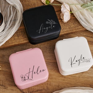 K&ouml;nnte beinhalten: Drei kleine quadratische Schmuckk&auml;stchen mit personalisierten Namen, "Angela", "Kayla" und "Helen", und floralen Designs. Die K&auml;stchen sind schwarz, wei&szlig; und rosa.