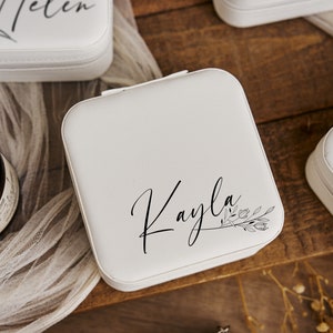 K&ouml;nnte beinhalten: Wei&szlig;e Schmuckschatulle mit floralem Design und dem Namen "Kayla" in Kursivschrift.