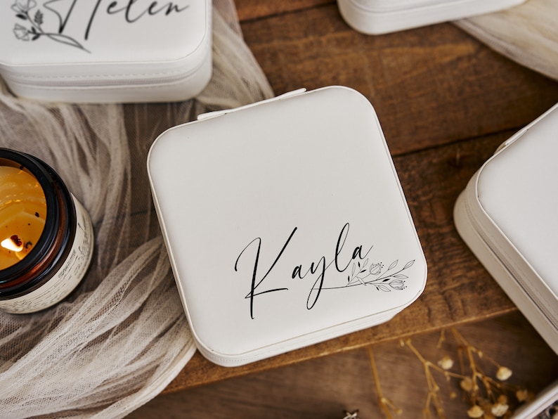 K&ouml;nnte beinhalten: Wei&szlig;e Schmuckschatulle mit floralem Design und dem Namen "Kayla" in Kursivschrift.