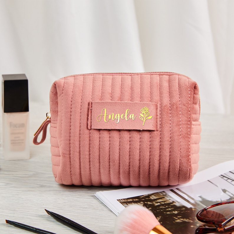 May include: A pink quilted makeup bag with a gold zipper and a gold label that says "Angela" with a small flower design.