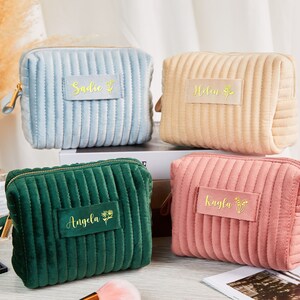 May include: Four quilted velvet cosmetic bags with gold zipper pulls and personalised names. The bags are in blue, beige, green, and pink.