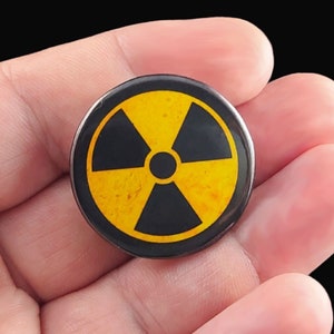 A black and yellow radiation warning symbol on a round pinback button.  Pins are 1.25" or 32mm round.  Metal Backing. Handmade in the USA. Not safe for children due to the sharp pin on the back. Brought to you by Brain Shudder Studio.