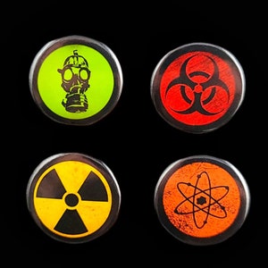 Four circular hazard warning button pins with distressed textures. gas mask silhouette on green. biohazard symbol on red. atom symbol on orange. radiation symbol on yellow. These represent various scientific and safety warning symbols commonly used to indicate dangerous materials or environments. Pins are 1.25" or 32mm round.  Metal Backing. Handmade in the USA. Not safe for children due to the sharp pin on the back. Brought to you by Brain Shudder Studio.
