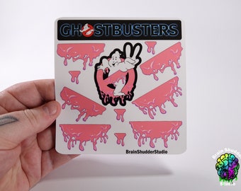 May include: A sticker sheet featuring the Ghostbusters logo with a pink slime dripping effect. The sheet includes the logo, a ghost figure, and several slime drips. The sticker sheet is labeled "Ghostbusters" and "BrainShudderStudio".