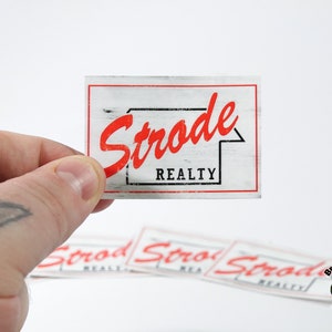 May include: A white sticker with a red and black logo that says "Strode Realty" on a woodgrain background.