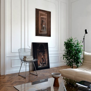 Peut inclure: Un int&eacute;rieur de salon avec des murs blancs, un parquet et une chaise en fil m&eacute;tallique noir. Il y a deux tableaux encadr&eacute;s au mur, l'un avec une porte en bois brun et l'autre avec une photo en noir et blanc d'une femme debout dans une porte. Une plante en pot se trouve dans le coin de la pi&egrave;ce, et un canap&eacute; blanc se trouve au premier plan.