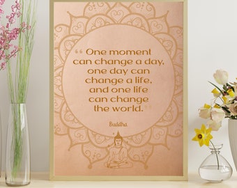 May include: A framed print featuring a quote by Buddha. The text, in brown, says: "One moment can change a day, one day can change a life, and one life can change the world." The background is a light peach colour with a mandala design.