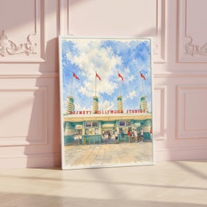 May include: A framed watercolor painting depicting the entrance to Disney's Hollywood Studios. The artwork features the iconic ticket booths, four tall towers with red flags, and a bright blue sky with clouds. The text reads Disney's Hollywood Studios.