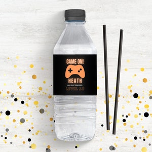 Puede incluir: Una etiqueta de botella de agua negra y naranja con el texto "Game On! Heath ha alcanzado el nivel 10" y un icono de mando de juego.