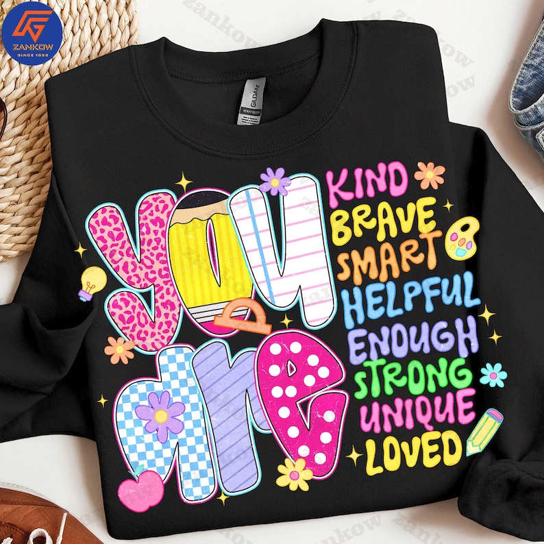 May include: Black sweatshirt with the words "YOU ARE" in colorful, patterned letters. The words "KIND, BRAVE, SMART, HELPFUL, ENOUGH, STRONG, UNIQUE, LOVED" are also displayed in a vertical arrangement. The design includes stars, flowers, and a pencil.