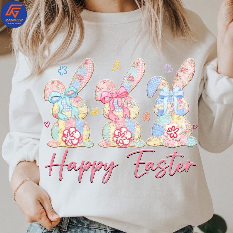 May include: White sweatshirt featuring three Easter bunny designs with floral patterns, bows, and patchwork details. The words "Happy Easter" are written in pink script below the bunnies. The design includes hearts and floral accents.