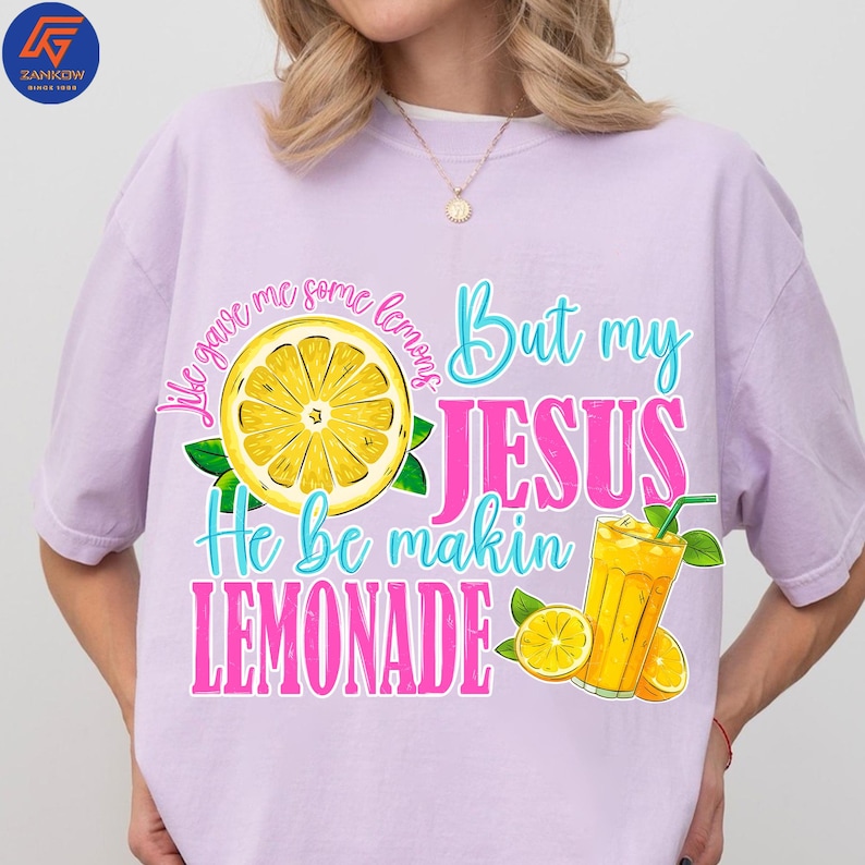 May include: A light purple t-shirt with the text "Life gave me some lemons But my JESUS He be makin LEMONADE" in turquoise and pink. The design includes a yellow lemon slice, green leaves, and a glass of lemonade.