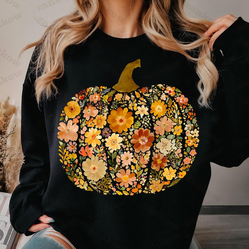 May include: Black sweatshirt featuring a floral pumpkin design. The pumpkin is composed of various flowers in shades of orange, yellow, and peach, with a green stem. The design is centered on the front of the sweatshirt.