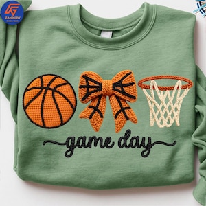 May include: Sage green sweatshirt with embroidered basketball, bow, and hoop designs. The basketball is orange with black lines, the bow is orange with black lines, and the hoop is brown with a white net. The words "game day" are embroidered in black.
