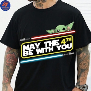 以下が含まれることがあります： 黒いTシャツ。Groguのグラフィックと「MAY THE 4TH BE WITH YOU」の文字。デザインには赤と青のライトセーバーと黄色のボーダーが含まれています。スターウォーズをテーマにしたTシャツ。