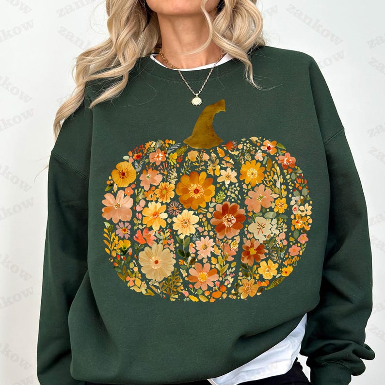May include: Dark green sweatshirt featuring a floral pumpkin design. The pumpkin is composed of various flowers in shades of orange, yellow, and peach, with a brown stem. The sweatshirt has a white crew neck.