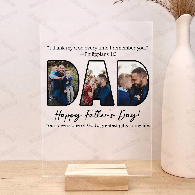 May include: A clear acrylic photo display with the word "DAD" cut out, each letter containing a family photo. The display includes the text "Happy Father's Day!" and a Bible verse. It rests on a wooden base.