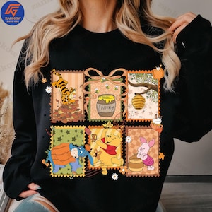 May include: Black sweatshirt with a colourful postage stamp design featuring Winnie the Pooh characters. The design includes Tigger, Eeyore, Winnie the Pooh, Piglet, a honey pot, and a beehive. The word "Hunny" is on the honey pot.
