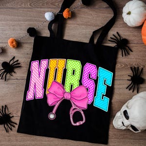 K&ouml;nnte beinhalten: Schwarze Tragetasche mit dem Wort "NURSE" in bunten karierten Buchstaben. Eine rosa Schleife und eine Stethoskop-Grafik befinden sich unter dem Wort. Der Hintergrund umfasst Halloween-Dekorationen wie Spinnen und K&uuml;rbisse.