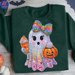 May include: Dark green sweatshirt featuring a rhinestone ghost with a rainbow bow, holding a pumpkin bucket and a drink. The ghost has a cute face and is covered in colorful rhinestones. Halloween-themed apparel.