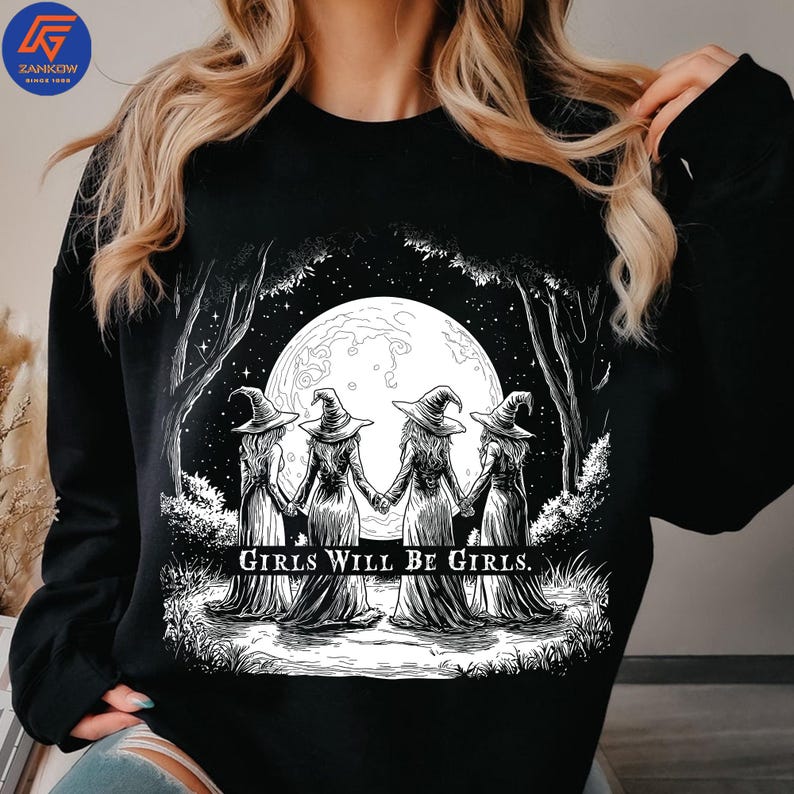 May include: Black sweatshirt featuring a graphic of four figures in witch hats holding hands in front of a full moon. The text "GIRLS WILL BE GIRLS" is printed below the figures. The ZANKOW logo is in the upper left corner.