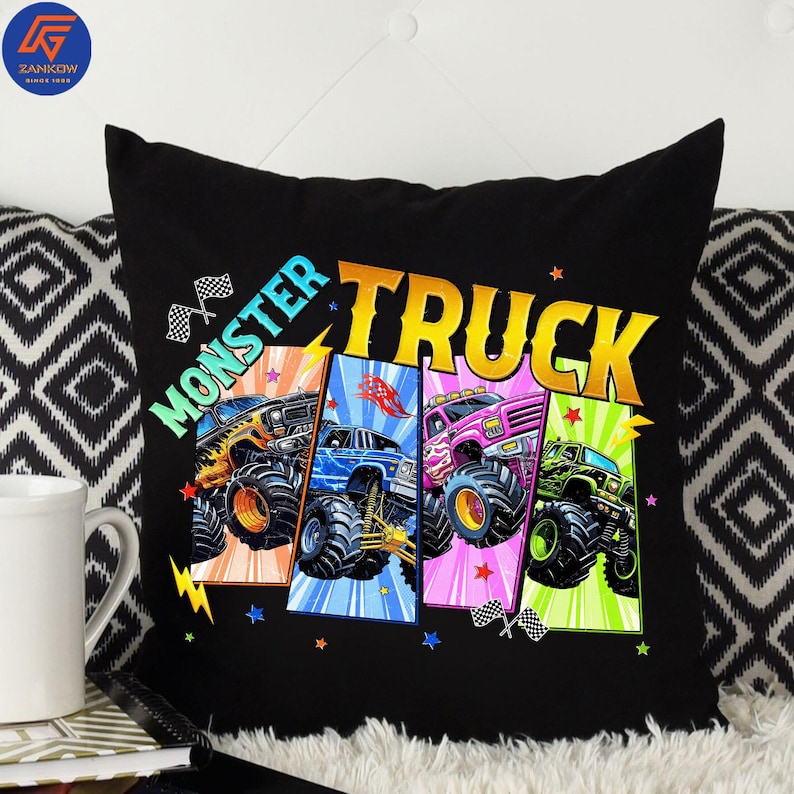 May include: Black throw pillow featuring a colorful graphic of four monster trucks. The pillow has the words "MONSTER TRUCK" in a vibrant design. Each truck is a different color, with checkered flags and stars.